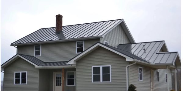 Two-story house with gray siding and metal roof under a cloudy sky.