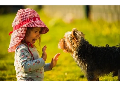 A joyful girl wearing a red sunhat plays with a small dog outdoors.