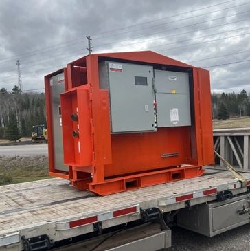 Large industrial orange electrical control panel on trailer bed outdoors.