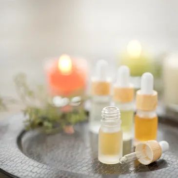 Essential oil bottles with droppers on a textured tray with a lit candle in the background.