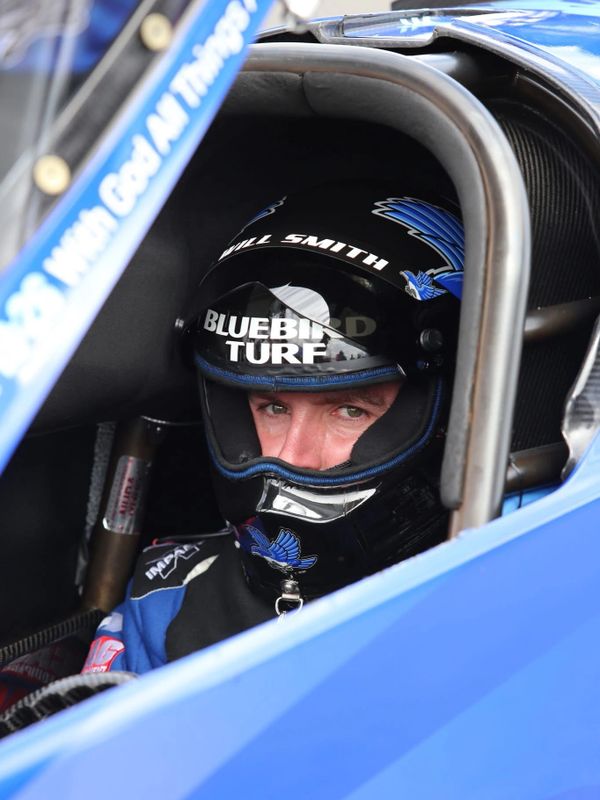 Race car driver Will Smith in a blue helmet inside a race car cockpit.