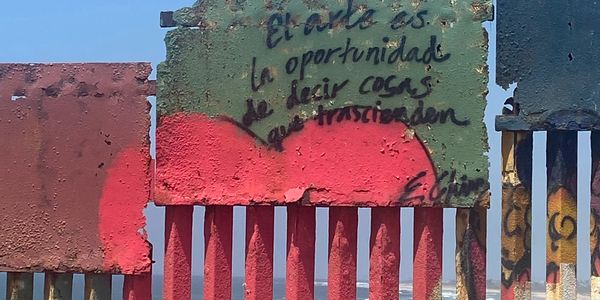 Graffiti with a message on a rusty metal fence painted red and green.