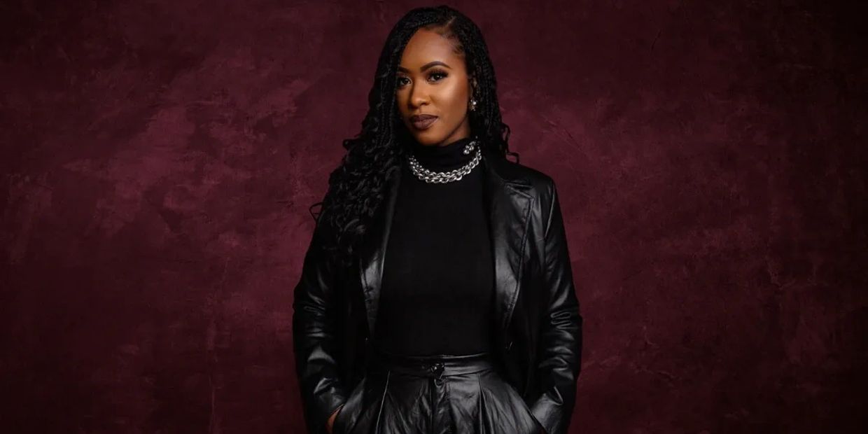 Confident woman in a black leather outfit against a dark maroon background.