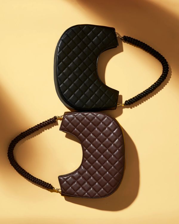 Two quilted handbags, one black and one brown, on a beige background.
