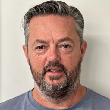 Middle-aged man with gray hair and beard in a blue shirt.