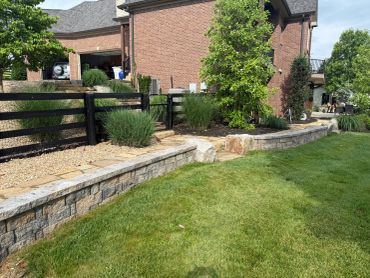 Neat stone retaining wall with green bushes and lawn.