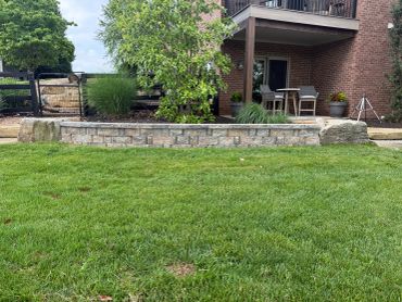 A backyard with green grass and a stone wall.