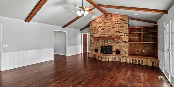 Residential den with a vaulted ceiling, exposed beams, and brick fireplace