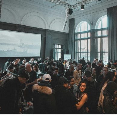 Crowded indoor event with people socializing in a high-ceiling room.