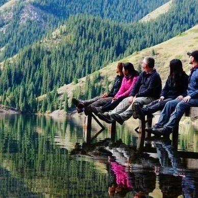 Five people sitting on a dock over a calm lake with forested hills in the background.