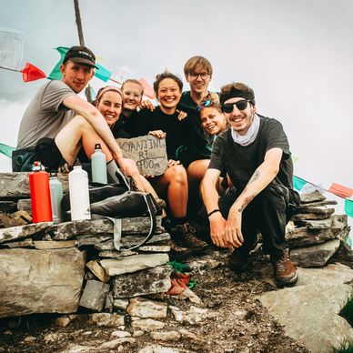 Group of hikers smiling with a handmade sign on rocky terrain.