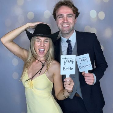 Happy couple in wedding attire holding 'Bride' and 'Groom' signs, smiling joyfully.