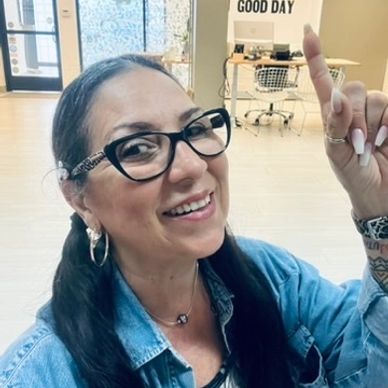 Smiling woman with glasses pointing up in a bright room.