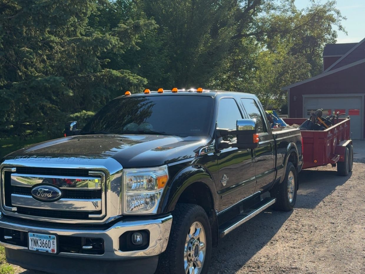 Black Ford Super Duty truck towing a red trailer loaded with equipment.