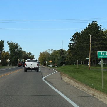 A white pickup truck driving on a rural road near Baldwyn city limits.
