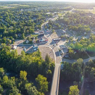 Aerial view of a small town with roads, buildings, and greenery under bright sunlight.