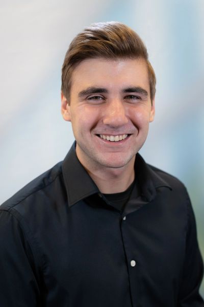 Young man with brown hair smiling, wearing a black shirt.