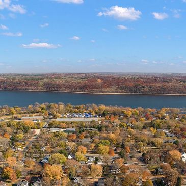 Aerial view of a suburban neighborhood by a wide river under a blue sky.