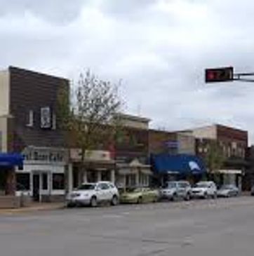 Street view of a small-town downtown with parked cars and storefronts.
