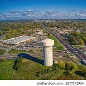 A water tower casting a long shadow near a busy intersection in a suburban area.
