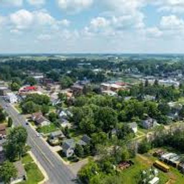 Aerial view of a small town with houses, trees, and roads under a partly cloudy sky.