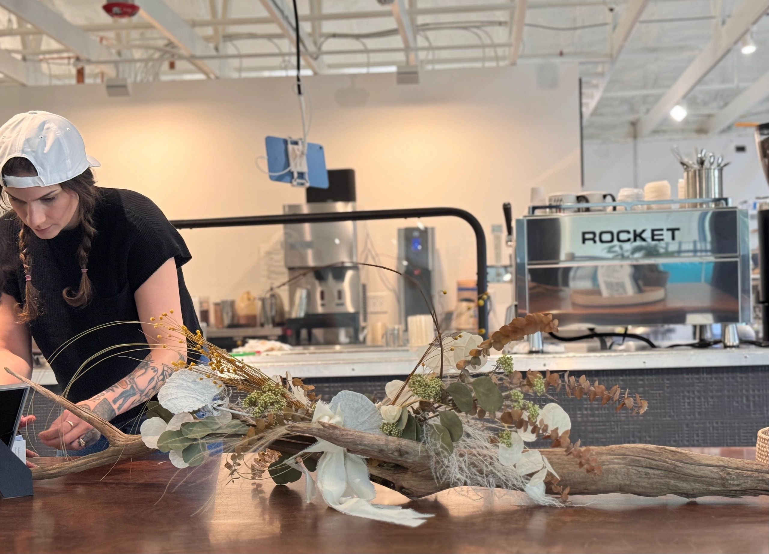 Woman working on floral arrangement in a modern cafe setting.