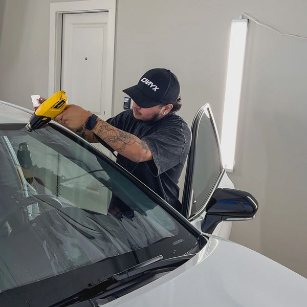 Man applying tint or film to a car windshield using a heat gun.