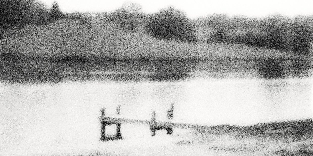 Grainy black and white image of a lakeside dock with trees in the background.