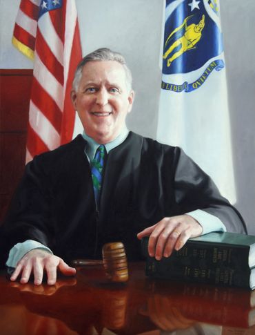 Portrait of a smiling judge in robes with gavel and law books.