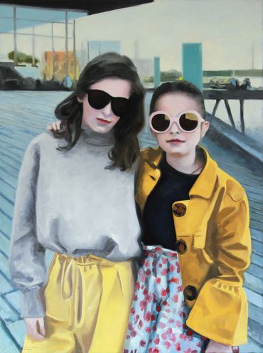 Two girls wearing sunglasses and colorful outfits stand together on a boardwalk.