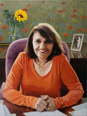Smiling woman in orange shirt sitting at a desk with sunflower and photo frame behind her.