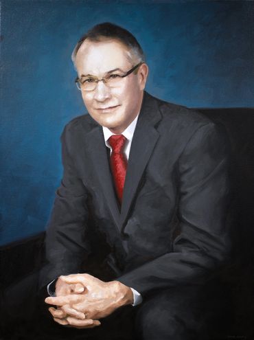 Portrait of a man in a suit with a red tie against a blue background.