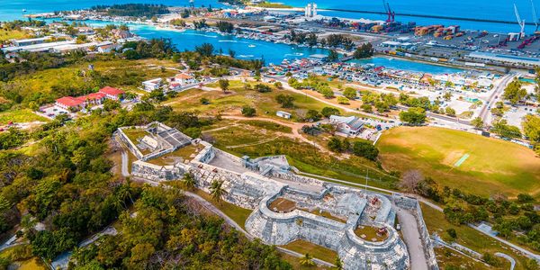 Aerial view of a coastal fortress and harbor with lush greenery and blue ocean.