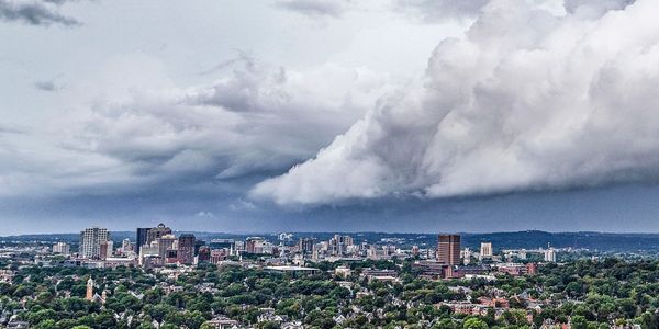 City skyline under dramatic cloudy sky with dense green trees.