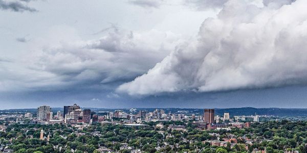 City skyline under dramatic cloudy sky with dense green trees.