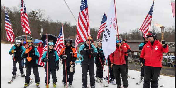 Group of skiers holding American flags and a Special Olympics flag on a snowy slope.