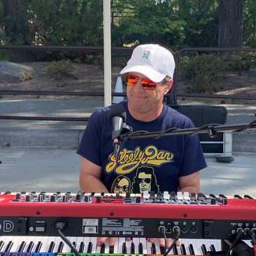 Man wearing sunglasses and a cap playing a keyboard outdoors.