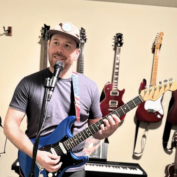 Man playing blue electric guitar and singing into microphone indoors.
