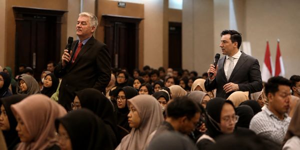 Two men speaking with microphones in a crowded room.
