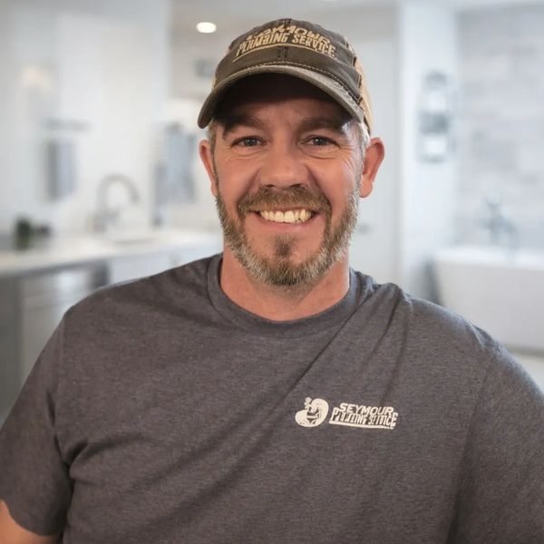 Smiling man in a Seymour Plumbing Service shirt and cap.