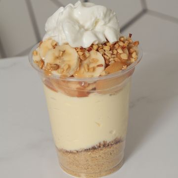 Cheesecake cup with banana, caramel, nuts, crumble, & whipped cream