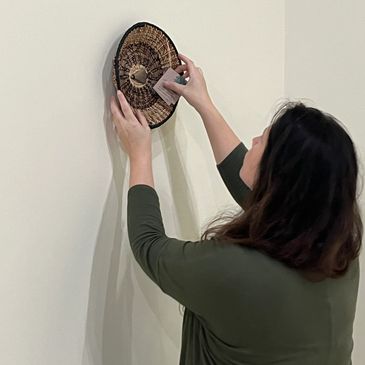 Brittany Taylor-Driggers hangs a pine needle basket on a gallery wall.