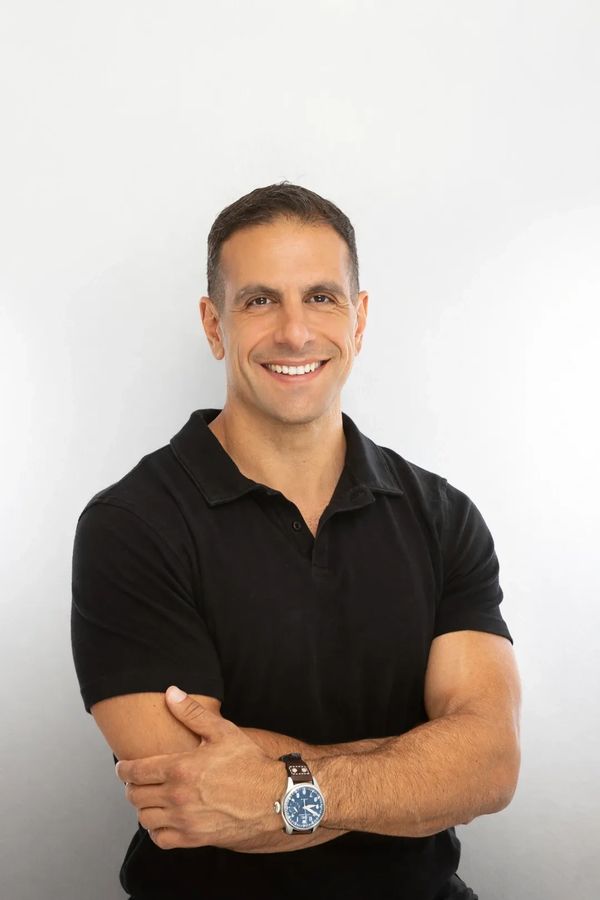Smiling man in black polo shirt with arms crossed against white background.