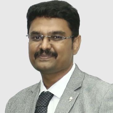Man wearing glasses, suit, and tie with a neutral background.