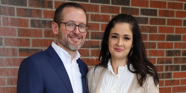 Smiling couple standing in front of a brick wall.