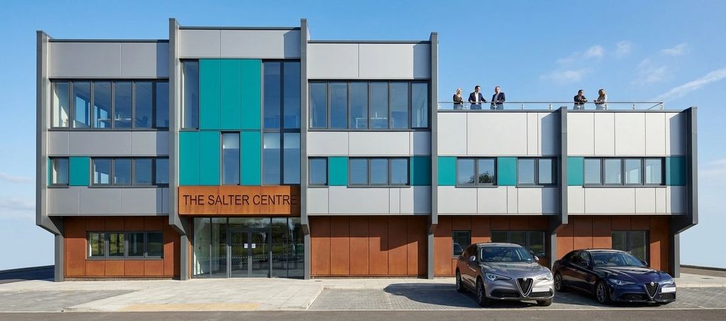 Modern office building with people on rooftop and two cars parked.