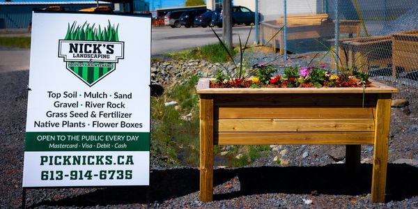 Sign advertising a landscaping depot beside a wooden planter box filled with flowers.