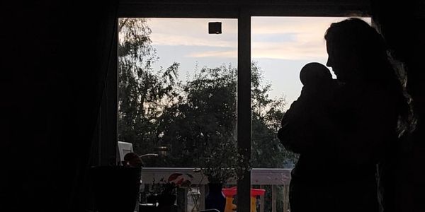 Silhouette of a person holding a baby near a window at dusk.