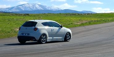 A white car driving on a race track with mountains in the background.