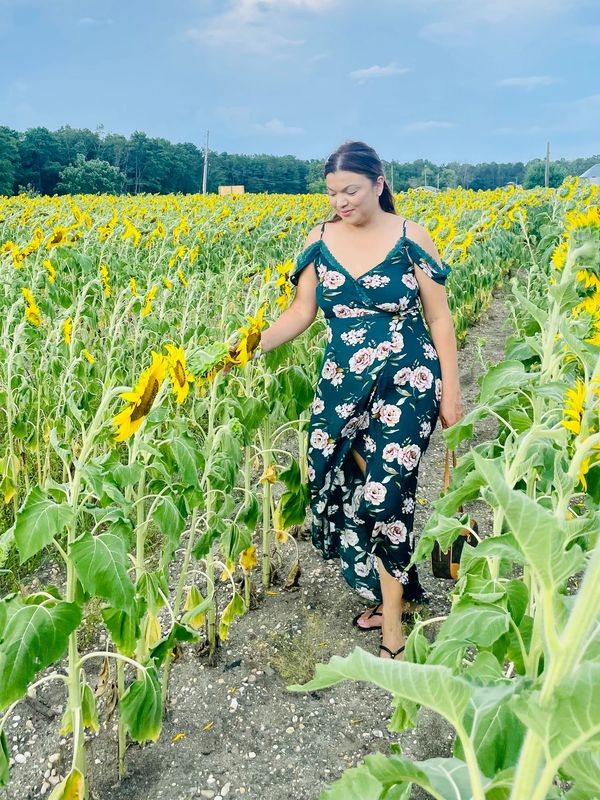 Woman in floral dress walks through a sunflower field on a cloudy day.